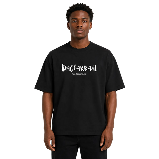 A man wearing a black oversized t-shirt with 'DAGGAKRAAL SOUTH AFRICA' printed in white across the chest, standing against a light gray background.
